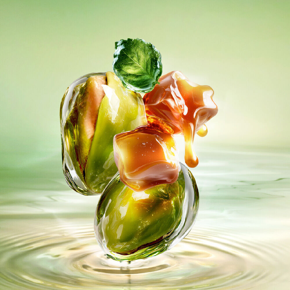 New Starlicious Pistachio Praline still life image featuring the slender bottle surrounded by its key ingredients: a patchouli leaf, whole pistachios, and dripping caramel cubes, all set against a luminous green rippling water background.