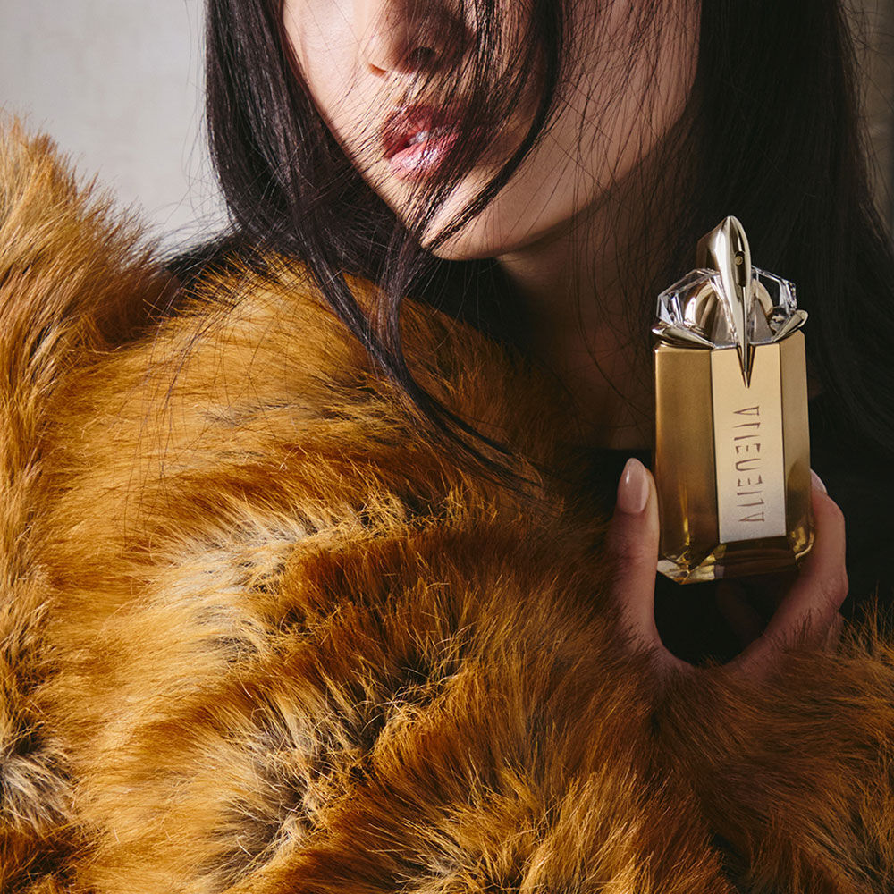 Model in a brown faux fur coat holding an Alien Goddess perfume bottle
