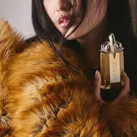 Model in a brown faux fur coat holding an Alien Goddess perfume bottle
