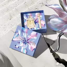 The Alien Goddess gold bottle centered amidst a dynamic splash of liquid gold and vanilla orchids, evoking a sense of divine solar strength.