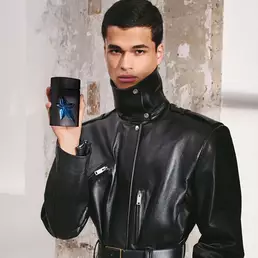 Male model in black leather jacket holding A*Men Eau de Toilette bottle against textured background.
