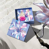 Mugler Mother's Day 2026 gift box with a kaleidoscopic floral pattern, containing the Alien Pulp perfume set on a sunlit stone surface with a concrete crack.