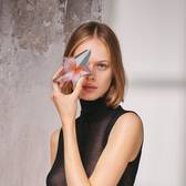 Portrait of a woman with short blonde hair holding the nude-toned Angel Blush star bottle in front of her eye, embodying pure glamour and an intimate glow.