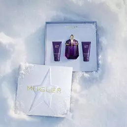 An open, textured ice-blue glistening Mugler gift set resting on snow, revealing an alien eau de parfum 30ml gift set