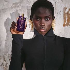 Person holding Mugler Alien purple perfume bottle against textured wall