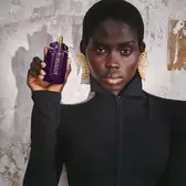 Person holding Mugler Alien purple perfume bottle against textured wall