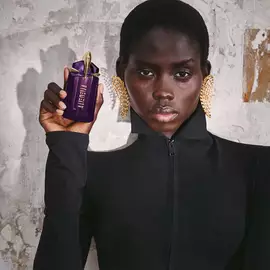 Person holding Mugler Alien purple perfume bottle against textured wall
