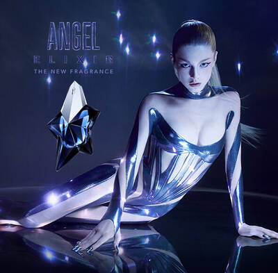 Hunter Schafer in a metallic body suit posing next to a bottle of Mugler Angel Elixir