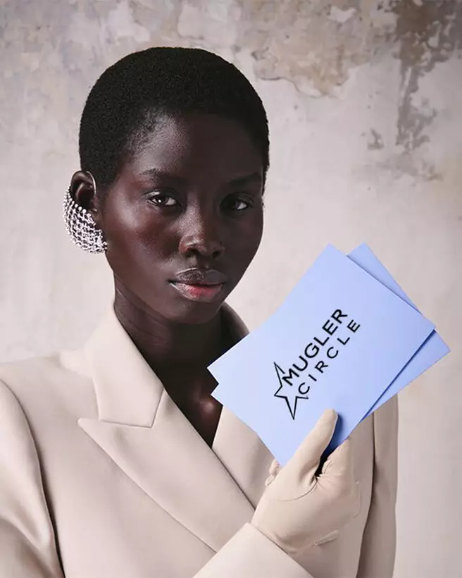 Close-up of a model holding light blue "Mugler Circle" loyalty program cards.