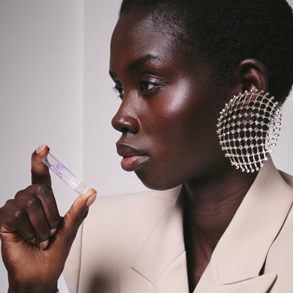 Model with silver mesh earring holding a small Alien by Mugler perfume vial in a beige blazer​