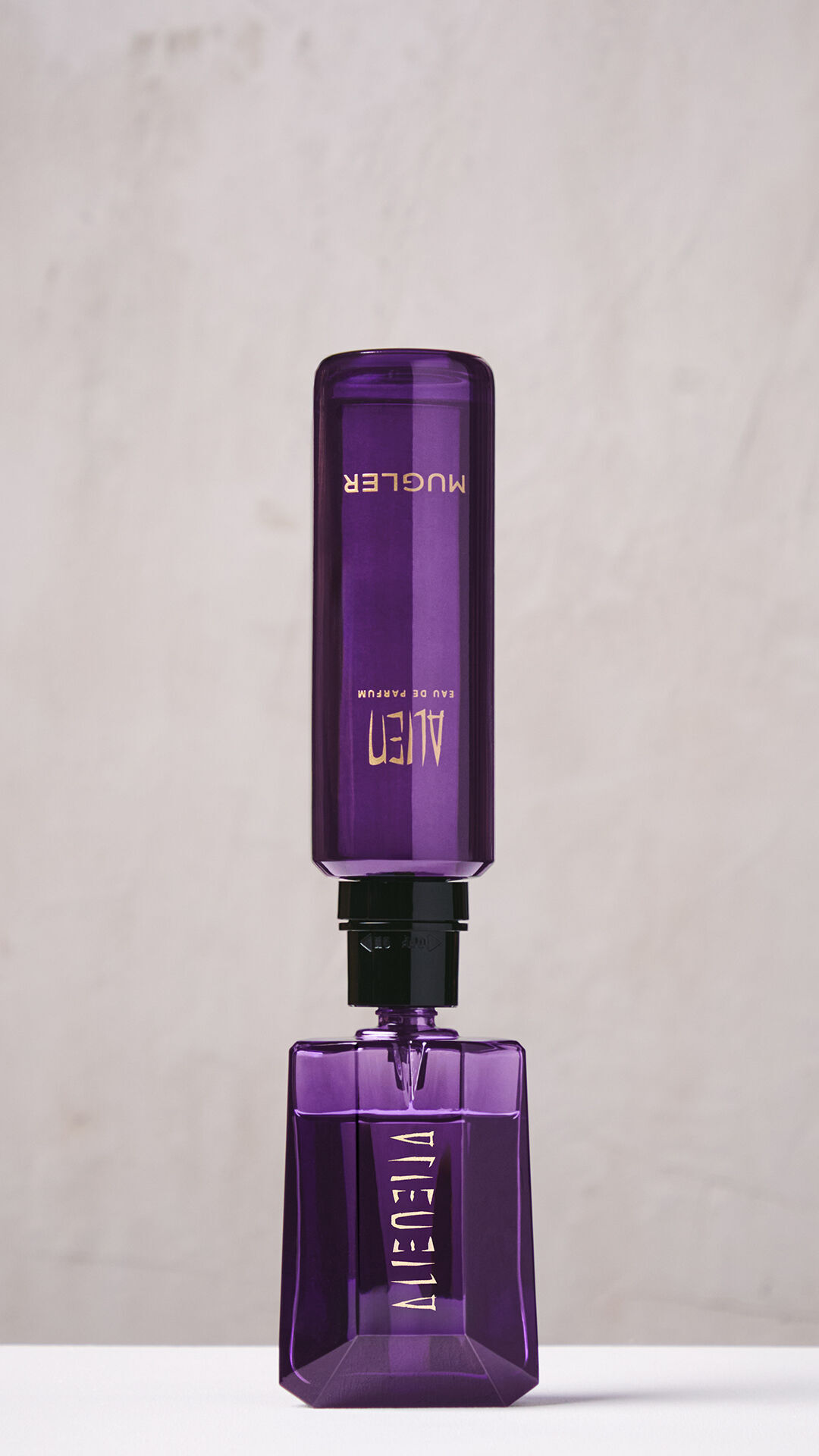 A hand refilling the purple Alien Eau de Parfum bottle using a purple refill bottle upside down.