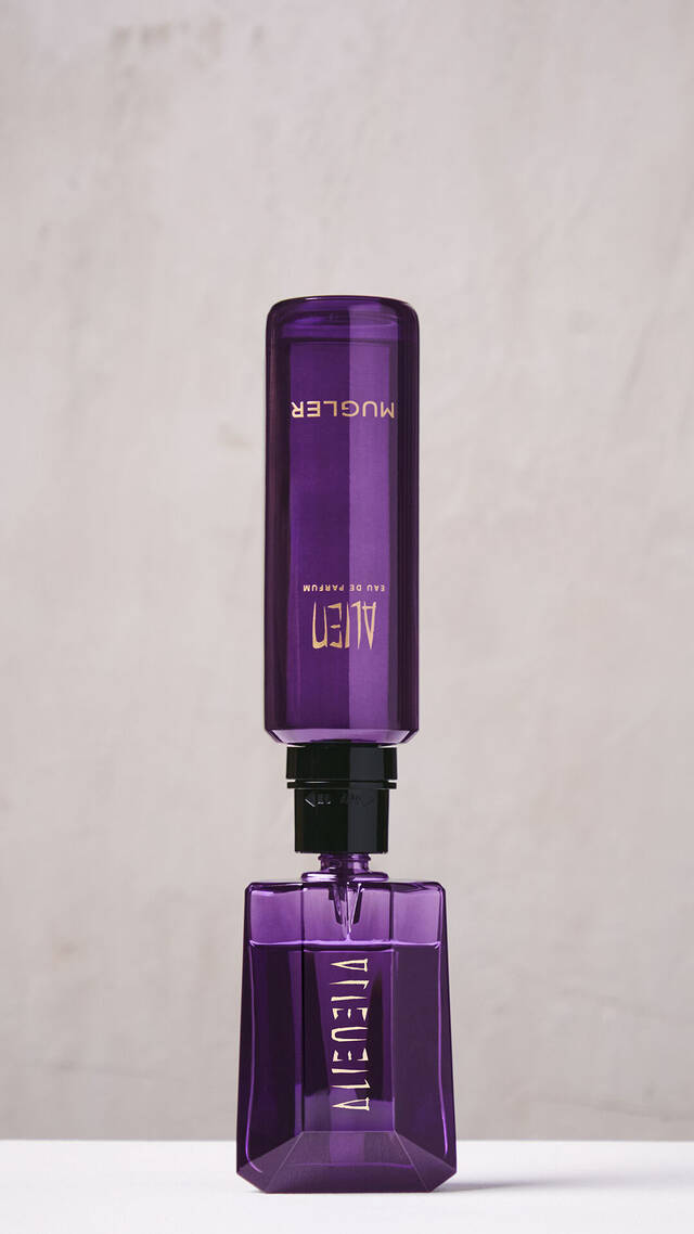 A hand refilling the purple Alien Eau de Parfum bottle using a purple refill bottle upside down.