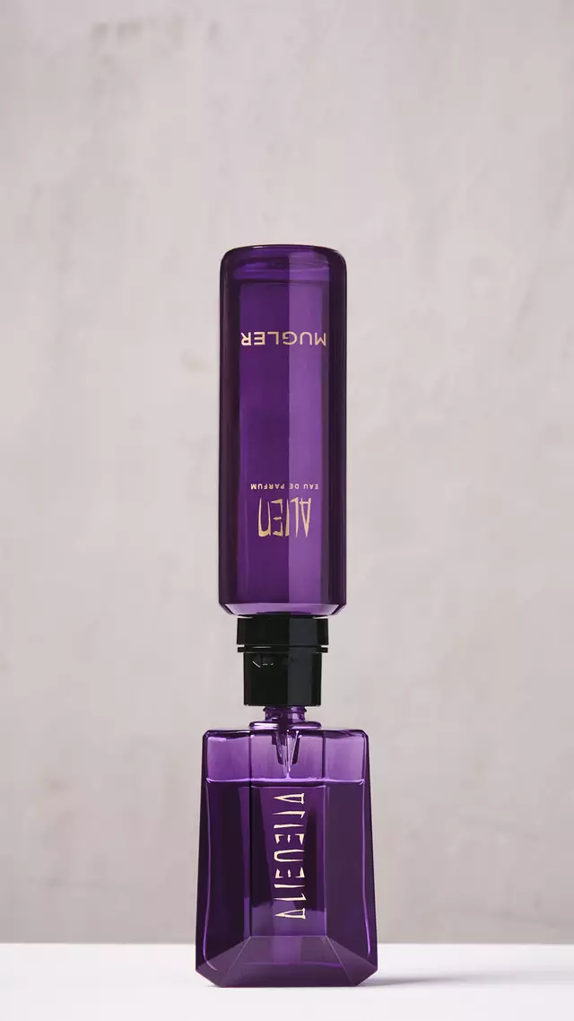 A hand refilling the purple Alien Eau de Parfum bottle using a purple refill bottle upside down.