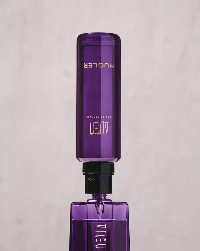 A hand refilling the purple Alien Eau de Parfum bottle using a purple refill bottle upside down.