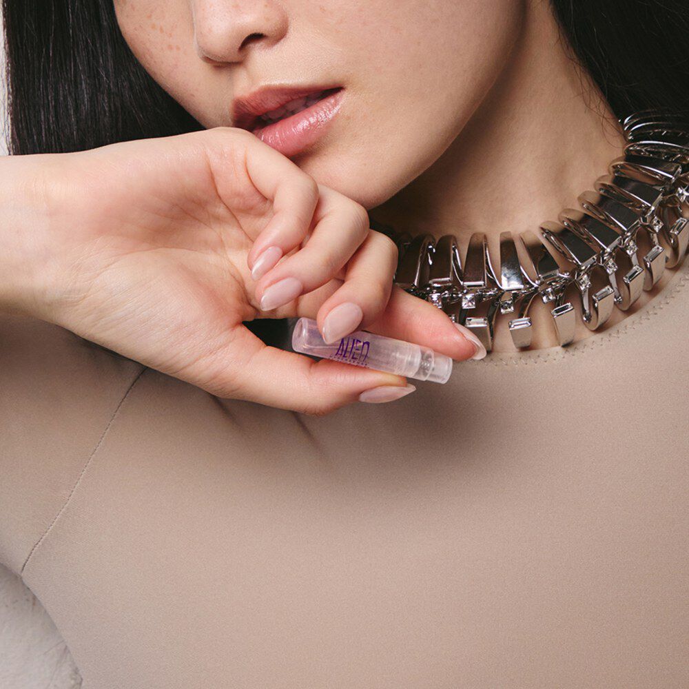 Close-up of model with silver chain necklace holding an Alien by Mugler perfume sample vial near her face​