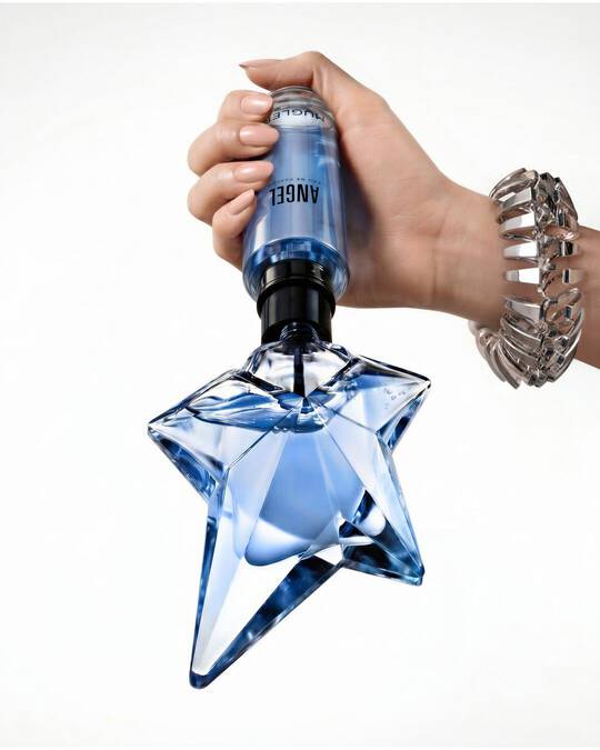 A hand holding the classic blue star-shaped Angel Eau de Parfum bottle pointing upwards against a plain white background.