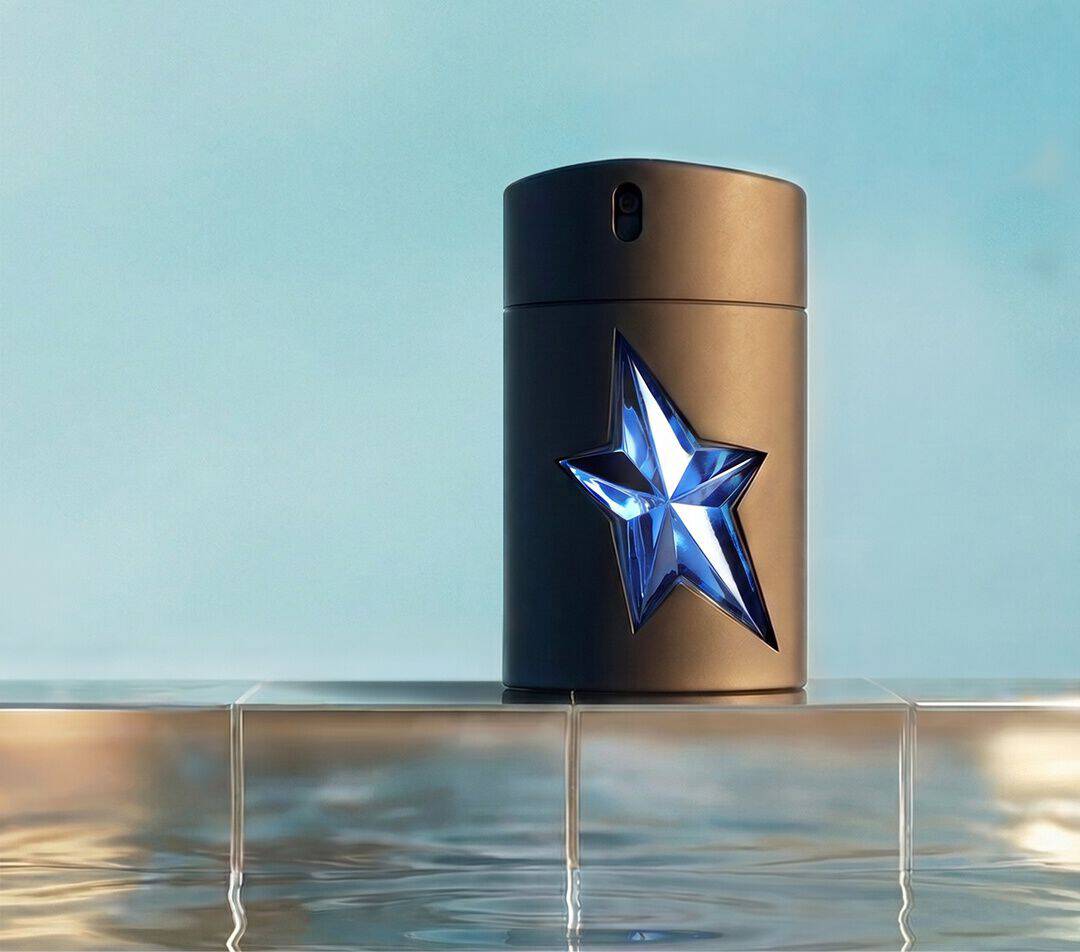 Mugler A*Men Eau de Toilette fragrance bottle with a faceted blue star detail placed on a tiled ledge above reflective pool water.