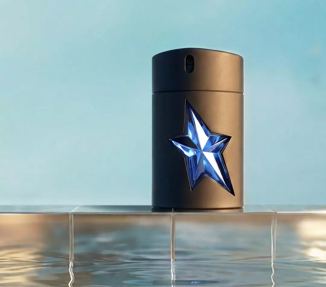 Mugler A*Men Eau de Toilette fragrance bottle with a faceted blue star detail placed on a tiled ledge above reflective pool water.
