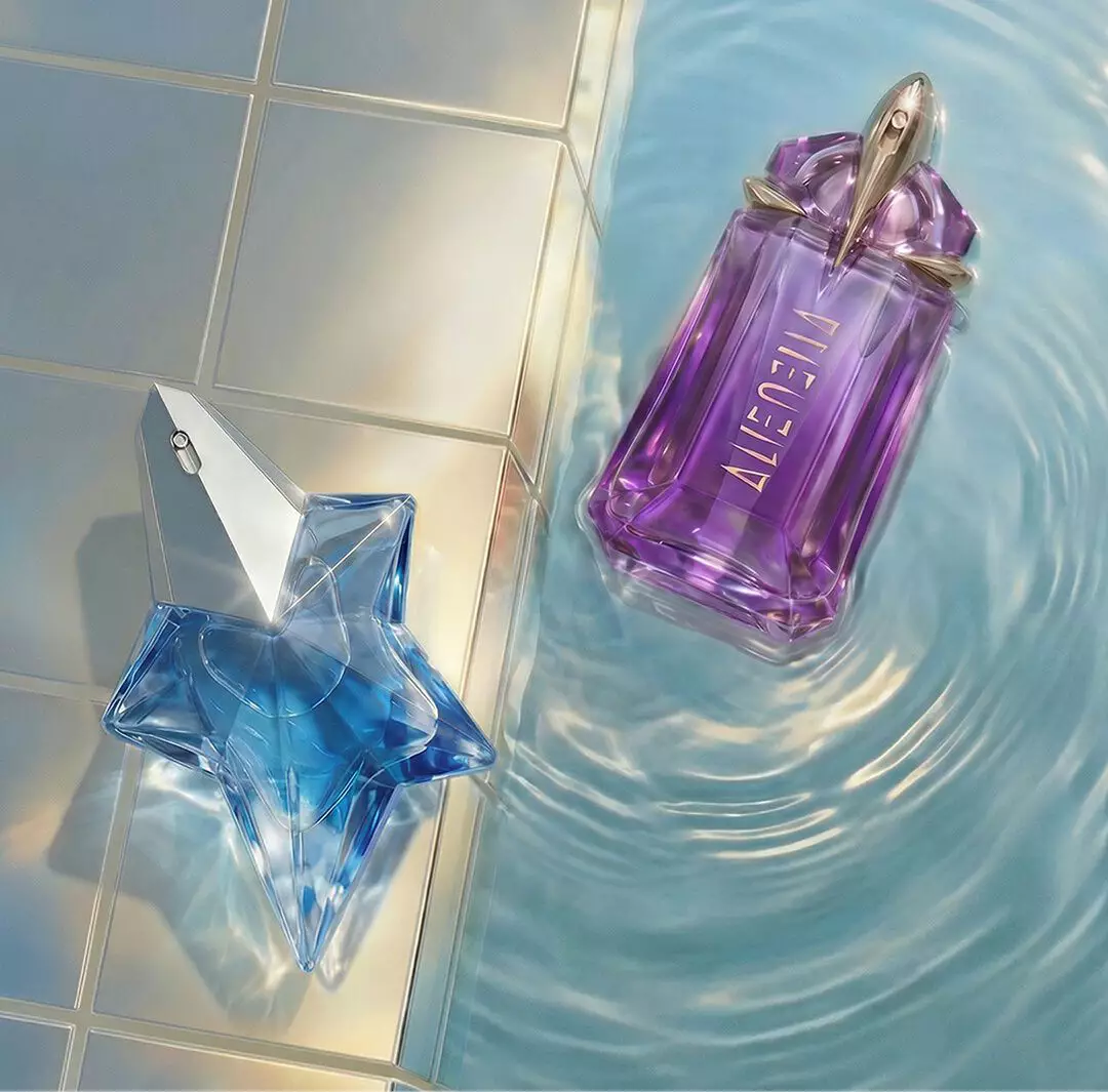 Mugler Angel Eau de Parfum shaped perfume bottle beside a purple Mugler Alien Eau de Parfum bottle floating in shimmering pool water next to pale tiles.