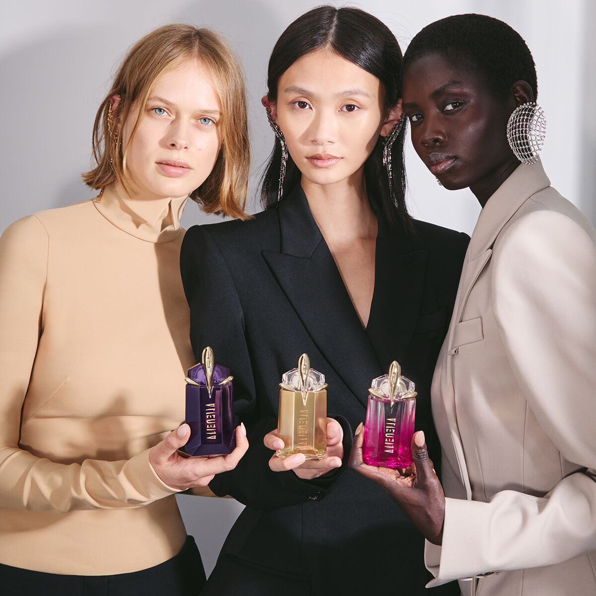 group of models holding mugler alien fragrance collection of engravable bottles
