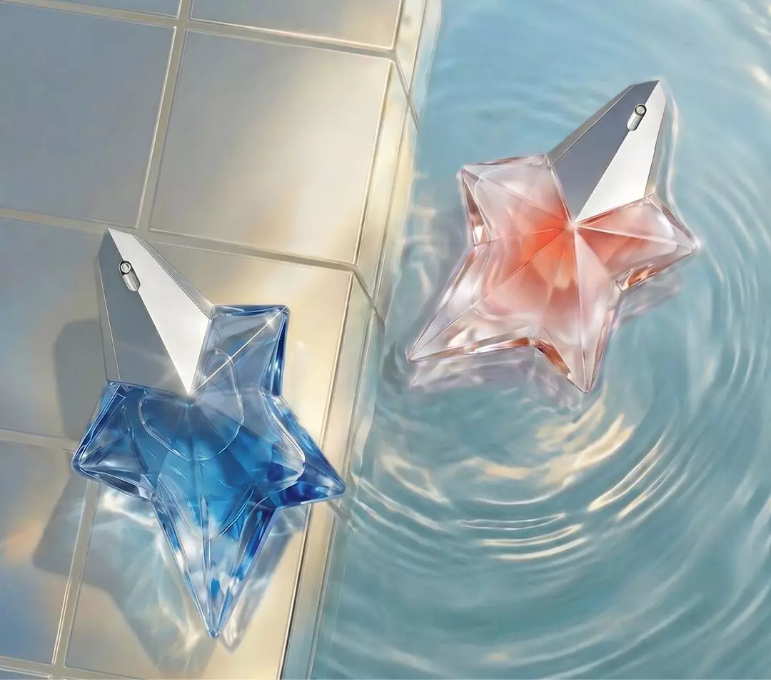 Blue and pale pink Mugler Angel Eau de Parfum and Angel blush star-shaped perfume bottles float in clear rippling water beside an iridescent tiled edge.