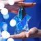 Two hands holding Mugler Angel eau de parfum shooting star bottle from top and bottom on blue background with blurry lights