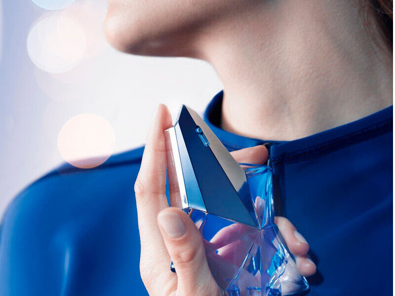 Zoomed in decolletage and hand holding Mugler Angel eau de parfum bottle