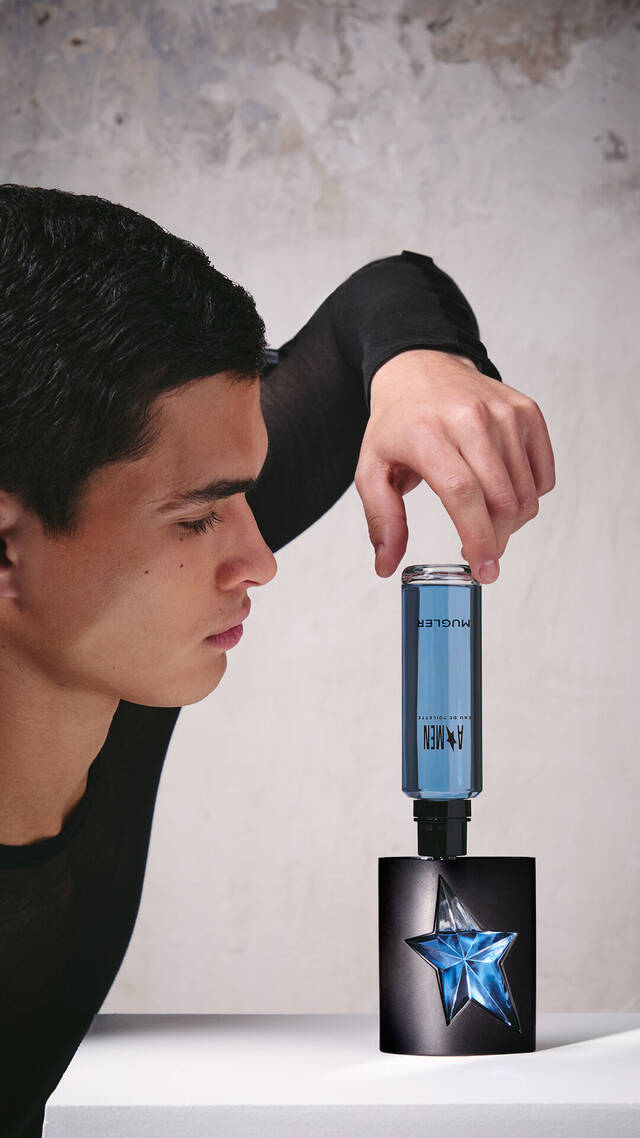A hand refilling the black and blue star A*Men Eau de Toilette bottle using a blue refill bottle upside down.
