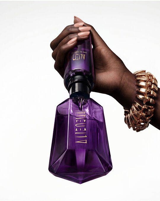 A hand holding the iconic purple Alien Eau de Parfum bottle against a plain white background.