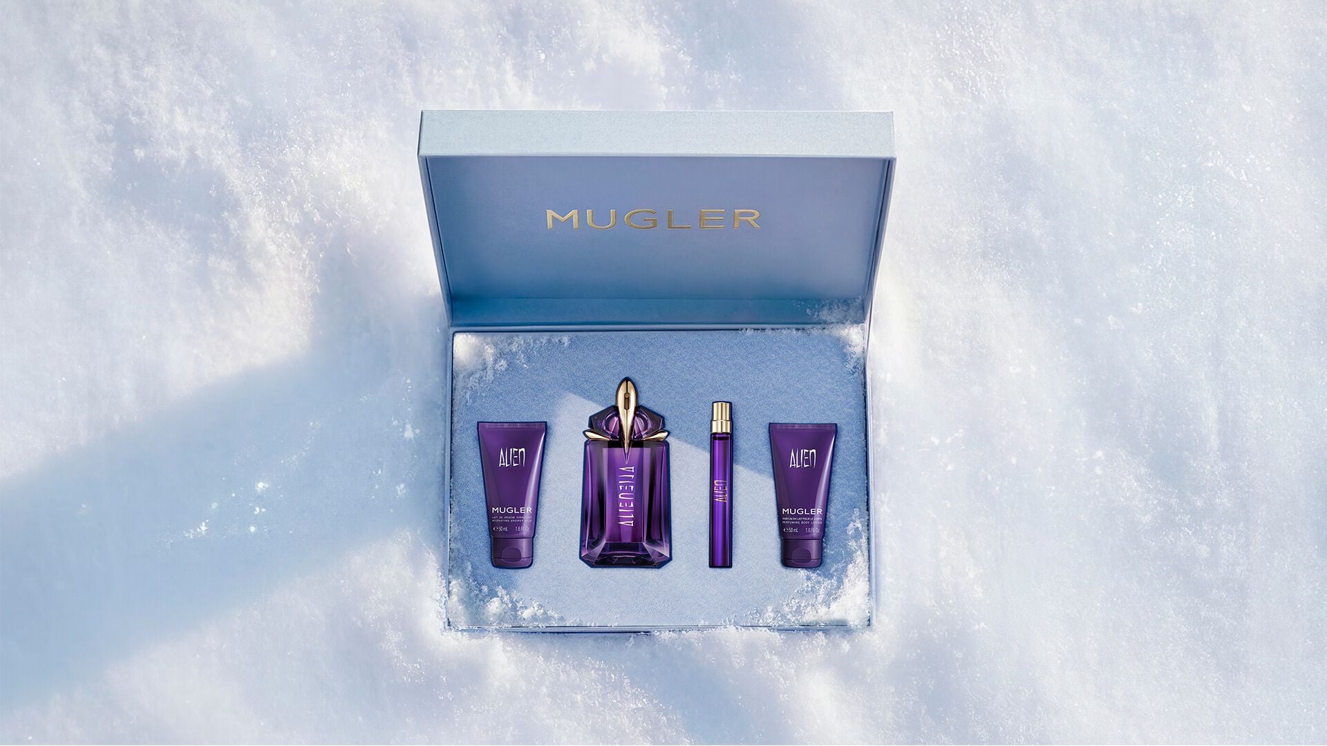 An open, textured ice-blue glistening Mugler gift set resting on snow, revealing an alien eau de parfum 60ml luxury gift set