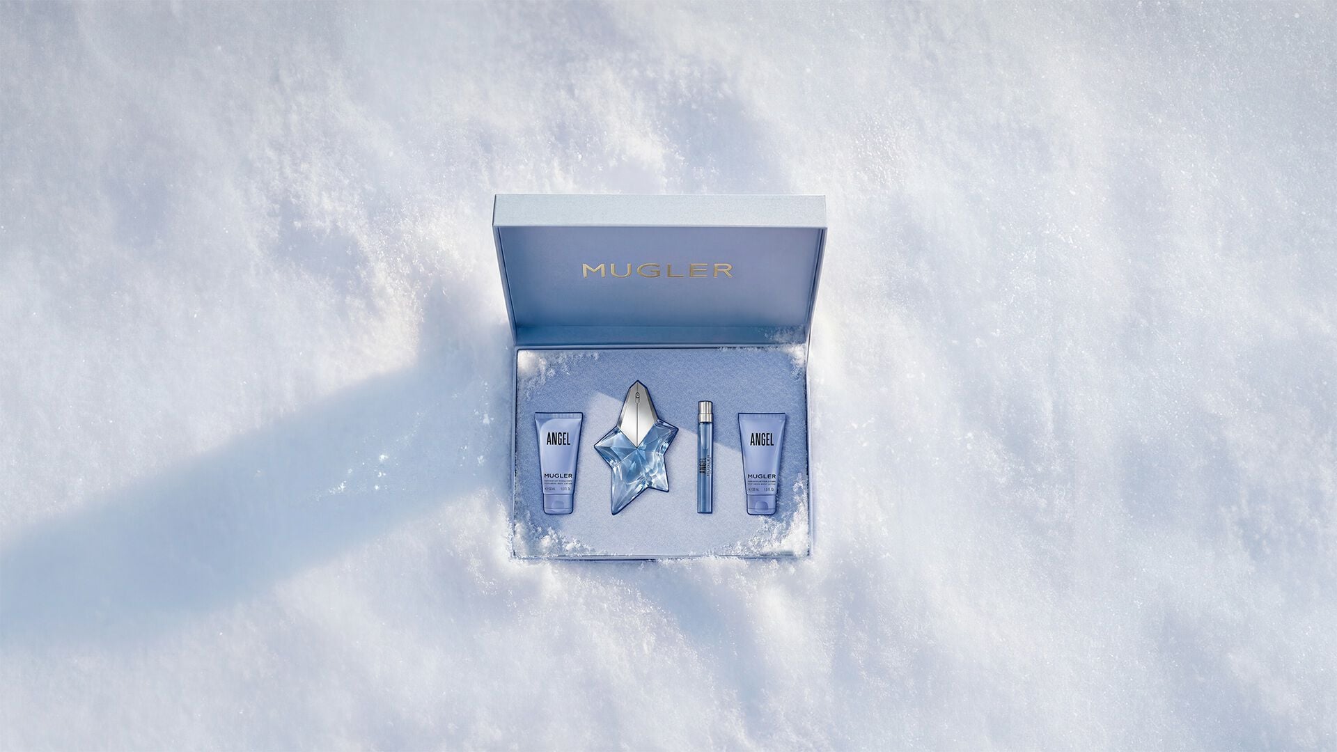 An open, textured ice-blue glistening Mugler gift set resting on snow, revealing an angel eau de parfum 50ml luxury gift set