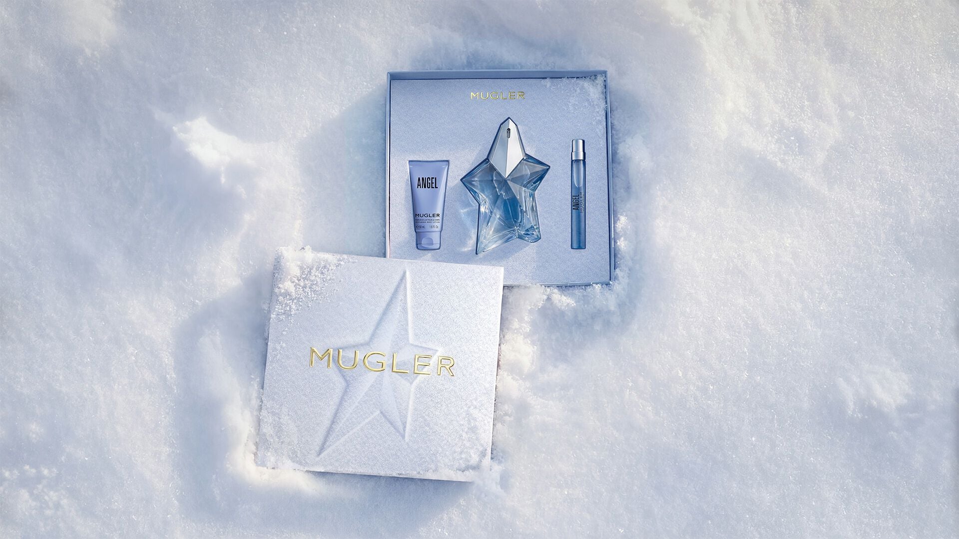 An open, textured ice-blue glistening Mugler gift set resting on snow, revealing an angel eau de parfum 100ml gift set