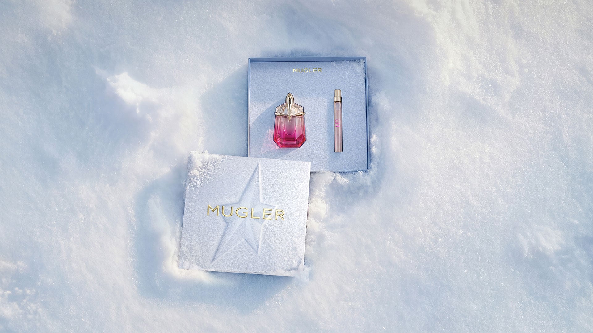 An open, textured ice-blue glistening Mugler gift set resting on snow, revealing an alien pulp eau de parfum 30 ml gift set. text reads "leave an unforgettable mark this holiday season with the fruity temptation of alien pulp wrapped in an elevated gift set