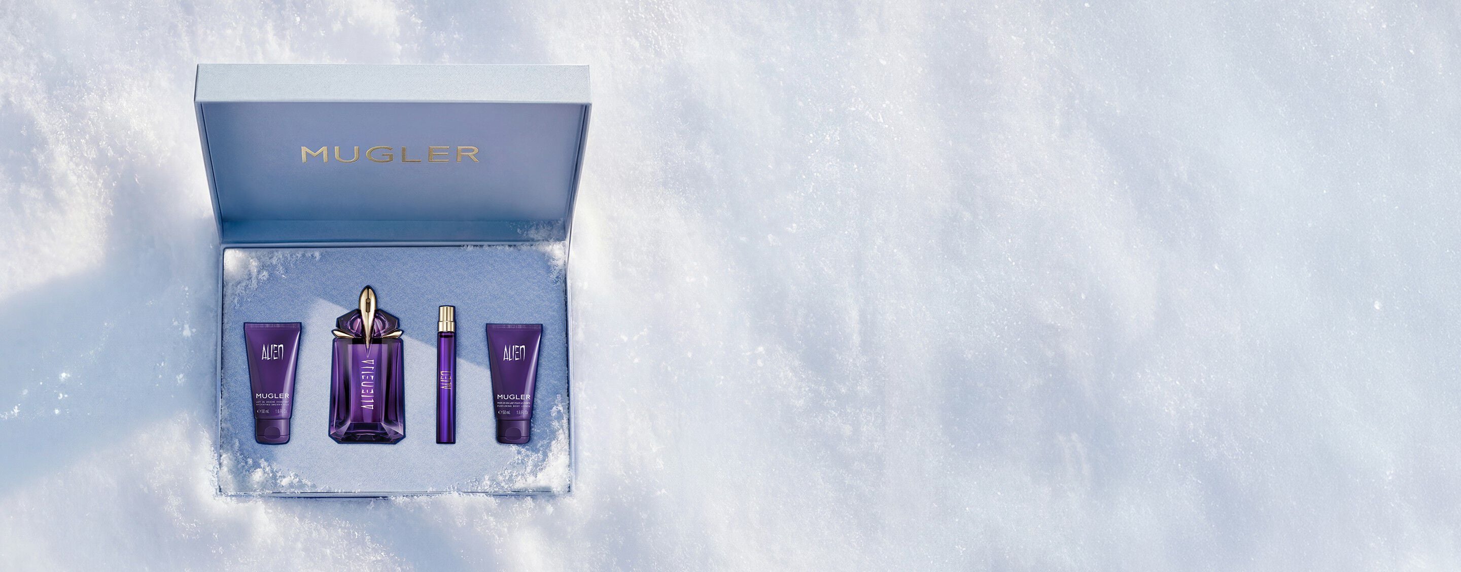 An open, textured ice-blue glistening Mugler gift set resting on snow, revealing an alien eau de parfum 60ml luxury gift set. text reads "offer a gift to remember this holiday season, with alien eau de parfum's powerful floral notes wrapped in a shiny gift set"