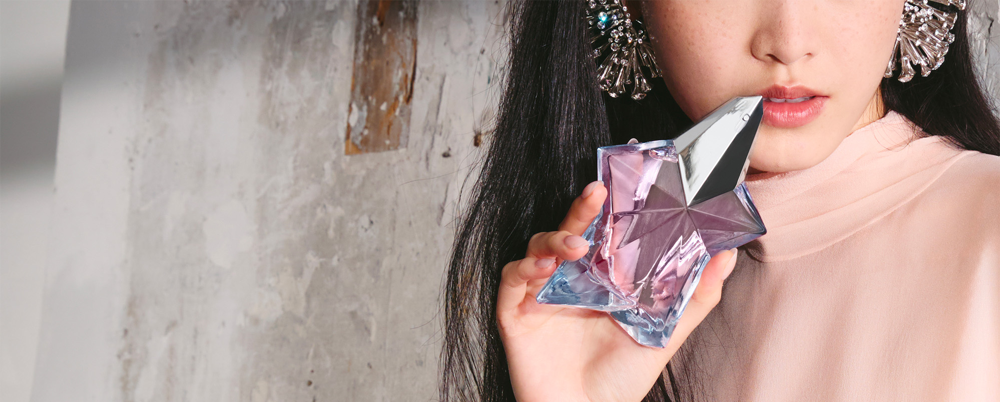 Woman holding Mugler Angel Eau de Toilette light pink transparent star-shaped bottle, fresh and feminine fragrance lifestyle shot
