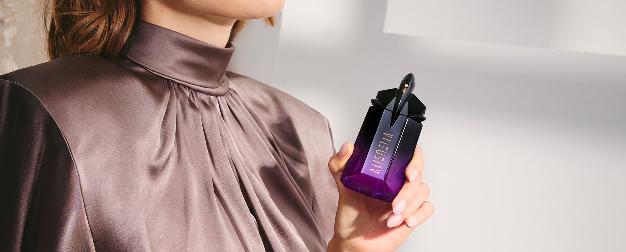 Elegant woman holding Mugler Alien Extraintense dark talisman-shaped bottle, intense luxury fragrance lifestyle shot